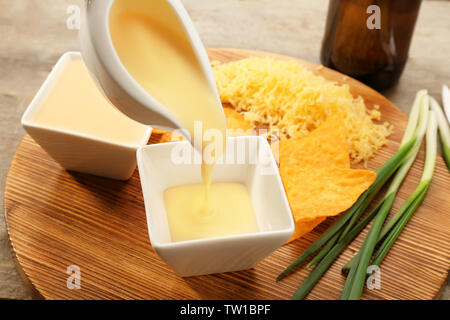 Pouring beer cheese dip into bowl on wooden stand Stock Photo