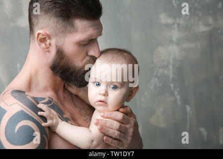 Handsome tattooed young man holding cute little baby on gray background Stock Photo