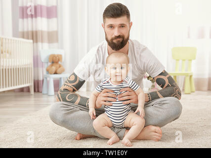 Handsome tattooed young man with cute little baby sitting on floor at home Stock Photo