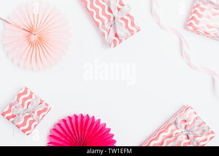 Pastel festive flat lay frame of pink gift boxes and paper decorations on white background. Stock Photo