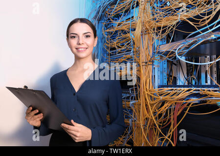 Beautiful young engineer with clipboard in server room Stock Photo