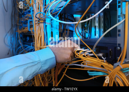 Hand of young engineer connecting cables in server room Stock Photo
