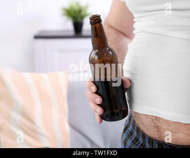 Man with big belly holding bottle of beer at home Stock Photo
