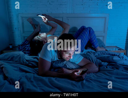 Sad man and woman married couple using their smart mobile phone in bed at night ignoring each other as strangers in relationship and communication pro Stock Photo