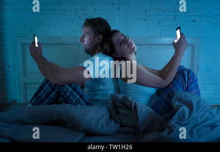 Sad man and woman married couple using their smart mobile phone in bed at night ignoring each other as strangers in relationship and communication pro Stock Photo