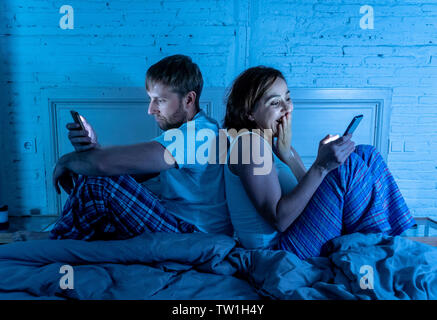 Couple in bed using phones, husband frustrated upset and unsatisfied while internet addict wife ignores him and enjoys mobile phone in social network Stock Photo