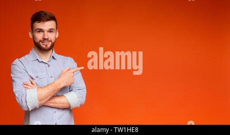 Young millennial guy looking at camera and pointing away on free space on orange background, panorama Stock Photo