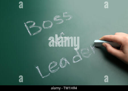 Female hand with chalk and words BOSS VS LEADER on chalkboard Stock Photo