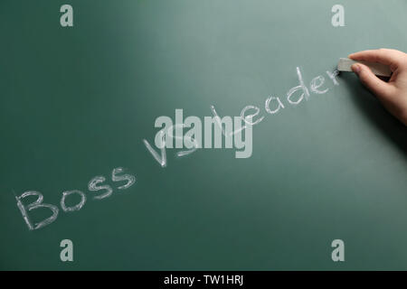 Female hand with chalk and words BOSS VS LEADER on chalkboard Stock Photo