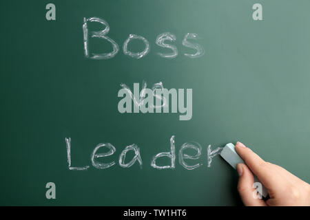 Female hand with chalk and words BOSS VS LEADER on chalkboard Stock Photo
