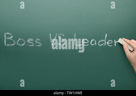 Female hand with chalk and words BOSS VS LEADER on chalkboard Stock Photo
