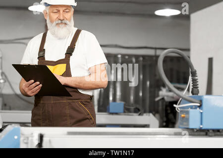 Front view of professional engineer working with plasma cutter and checking device on factory. Clever man in uniform and helmet and writing data. Concept of technology and production. Stock Photo