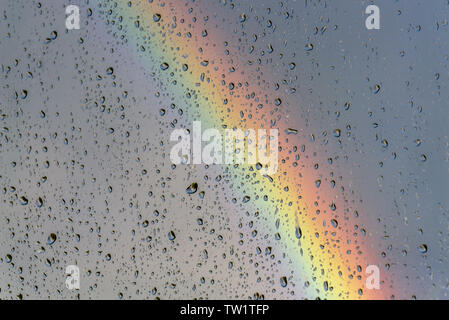 Beautiful bright rainbow on the background of a stormy blue sky through a window glass with rain drops Stock Photo