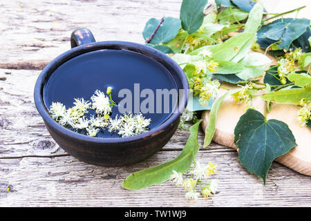 A cup of linden tea near the lime flowers on the background of old boards. linden flowers and a cup of tea. herbal tea. cold and flu remedy.