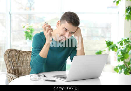 Young man using laptop and smoking cigarette Stock Photo
