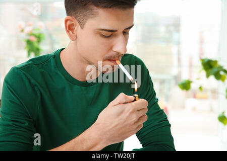 Young man lighting cigarette on blurred background Stock Photo