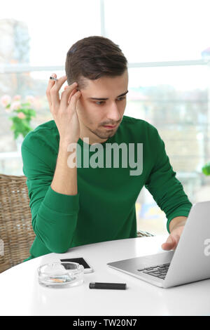 Young man using laptop and smoking cigarette Stock Photo