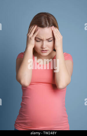Pregnant woman suffering from headaches on blue background Stock Photo