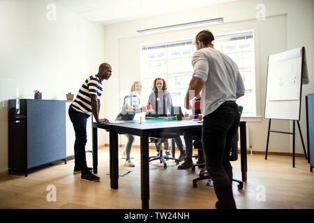 Laughing group of designers playing table tennis on a boardroom table while taking a break from their office meeting Stock Photo