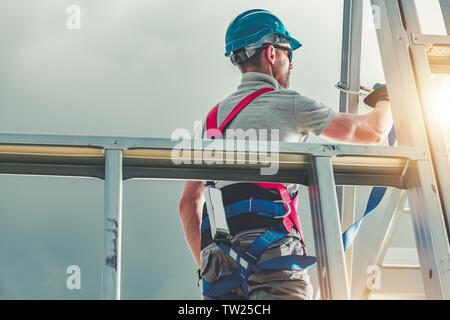 Caucasian Construction Contractor in His 30s Wearing Safety Harness. Steel House Building. Industrial Theme. Stock Photo