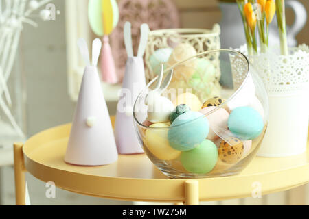 Glass vase with painted Easter eggs and handmade paper rabbits on table Stock Photo