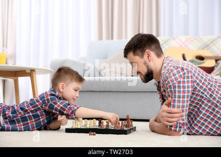 Father and son playing chess while lying on floor at home Stock Photo