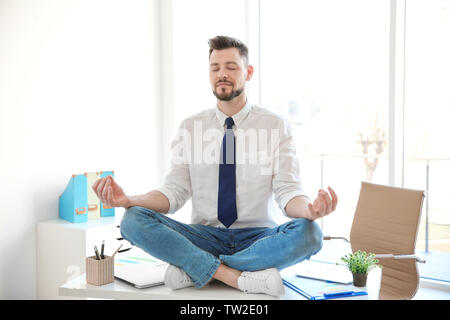 Young businessman sitting on table in office and meditating Stock Photo