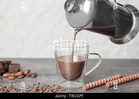 Pouring hot cocoa drink into glass cup on kitchen table Stock Photo