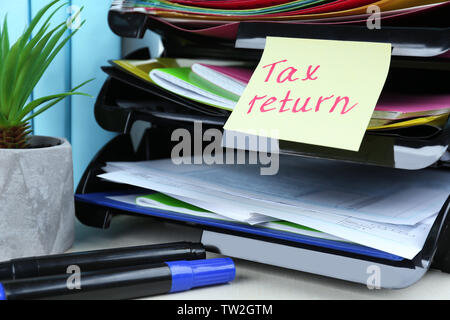 Note with TAX RETURN text, forms and stationery on table Stock Photo