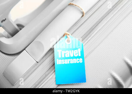 Grey suitcase with label, closeup. TRAVEL INSURANCE concept Stock Photo