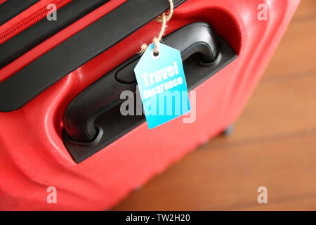 Red suitcase with label, closeup. TRAVEL INSURANCE concept Stock Photo