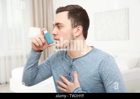 Young man using inhaler during asthmatic attack at home Stock Photo