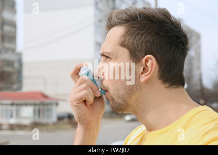 Young man using inhaler during asthmatic attack outdoors Stock Photo