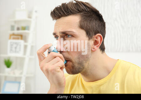 Young man using inhaler during asthmatic attack at home Stock Photo