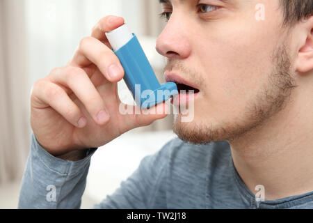 Young man using inhaler during asthmatic attack at home, closeup Stock Photo