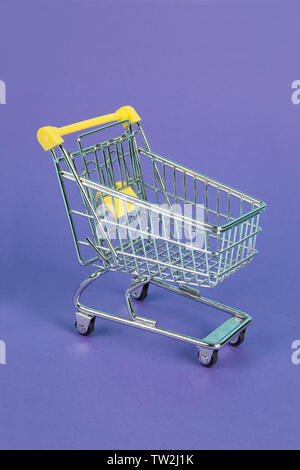 a mini cart on a purple background with a play of coloured light. Minimal color still life photography. Stock Photo