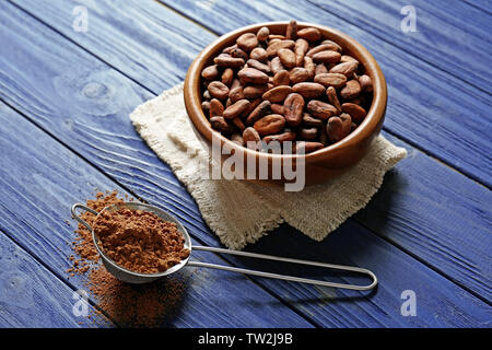 Cocoa beans in bowl and sieve with powder on wooden table Stock Photo