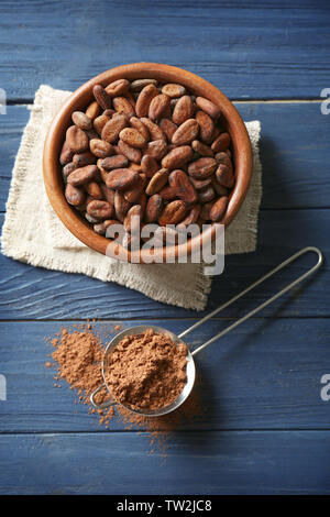 Cocoa beans in bowl and sieve with powder on wooden background Stock Photo