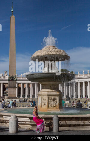 Lady in a red dress, sitting by the Fontana gemella del Bernini, sinistra in St Peters square, Rome with the Vatican obelisk Stock Photo