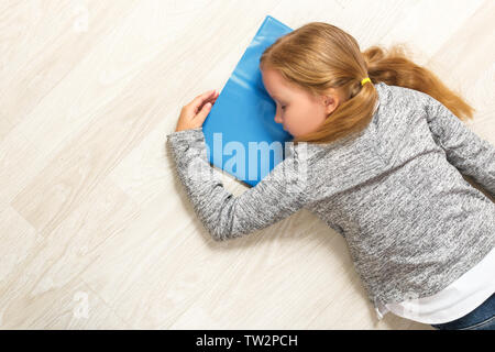 The little girl lies and sleeps on the floor. The child fell asleep while reading a book. Stock Photo