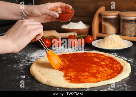 Female chef spreading sauce onto dough for pizza on table Stock Photo