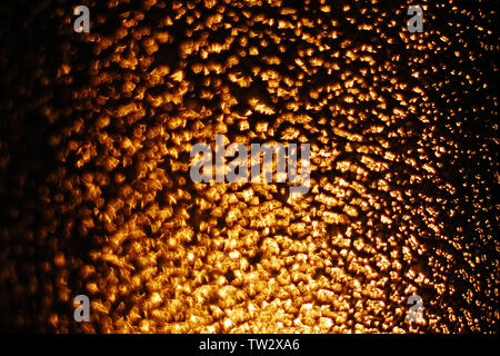 Abstract background of defocused golden highlights on brown background, light of setting sun through textured glass Stock Photo