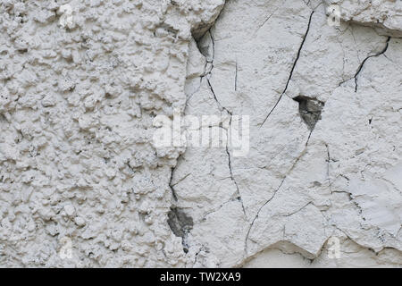 Extremely rough grungy texture of white plastered stone wall, half destroyed, chipped and cracked Stock Photo