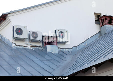 External units of modern air conditioning system next to old ventilation pipes on house roof Stock Photo