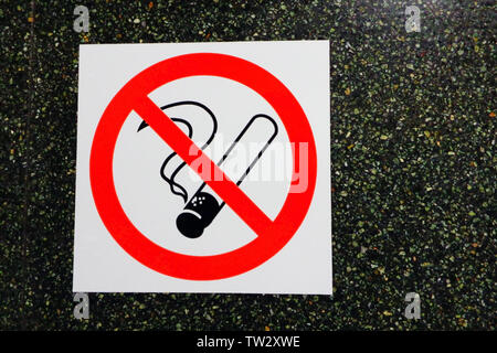 White sticker with red crossed circle on smoking cigarette against black marble office wall , no smoking icon on dark stone background, close up Stock Photo