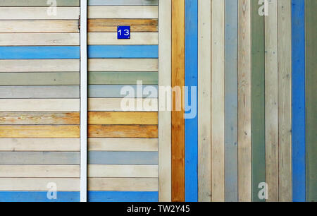 House wall and part door of wooden colorful partially faded boards arranged vertically and horizontally. Small blue sign with number 13 on it Stock Photo
