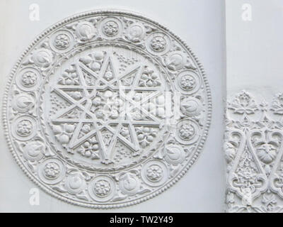 Molding on white wall, floral and geometric pattern with ten-pointed star inscribed in a circle, lines,curls, flowers and fruits, fantasy bas-relief Stock Photo