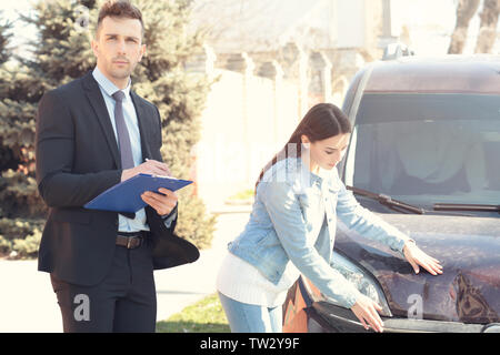 Loss adjuster and young woman inspecting car after accident Stock Photo