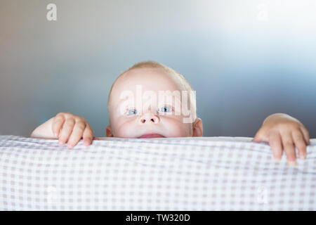 Little toddler boy playing on the bed. Cute kid smiling and hiding under cover. Palyful and mischievous eyes. Hide-and-seek. Children having fun playi Stock Photo