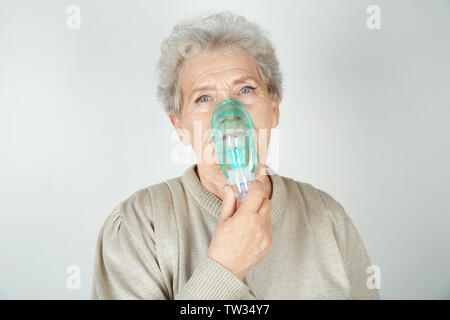 Elderly woman using asthma machine on light background Stock Photo